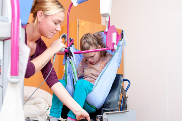 A disabled child is lifted into a wheelchair by a nurse using special needs lifting equipment